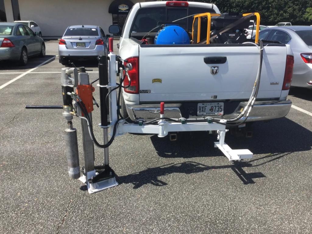 Hitch-mounted core drill rig on white Ram pickup truck